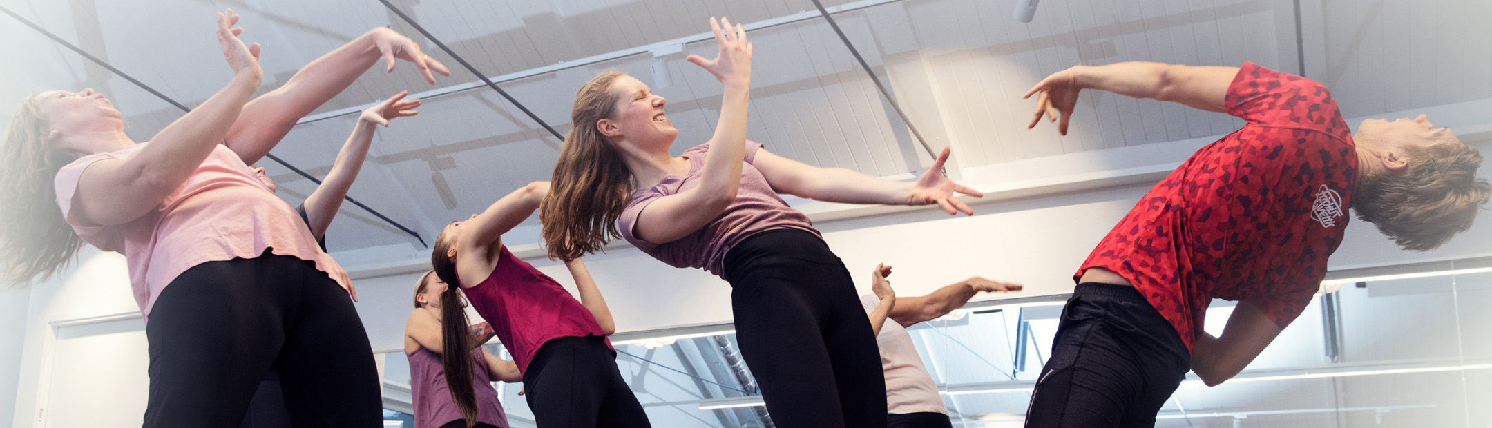 En grupp med rosa och röda tröjor som lutar sig bakåt i en dansövning